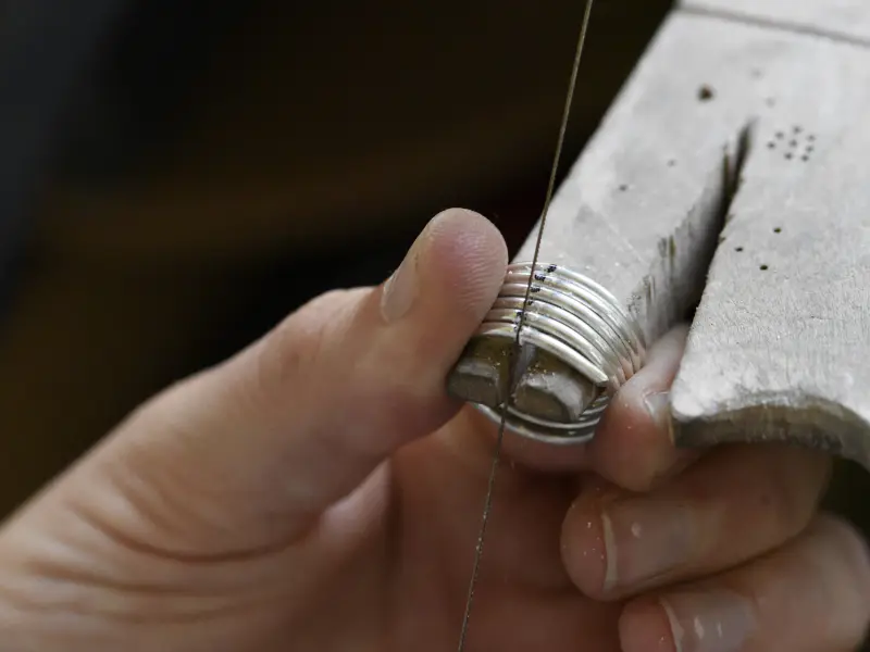 Sawing through a silver ring held against a bench pin