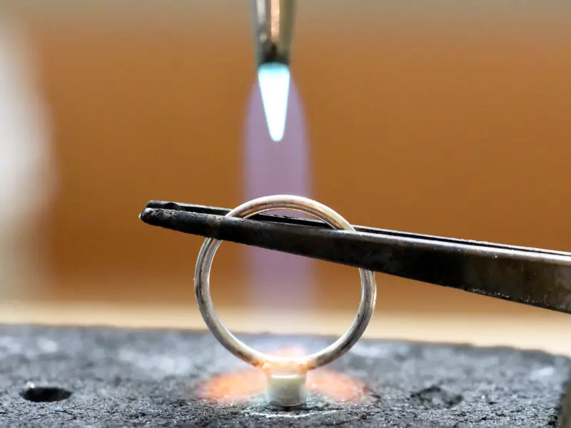 A torch flame soldering a silver ring on a charcoal block