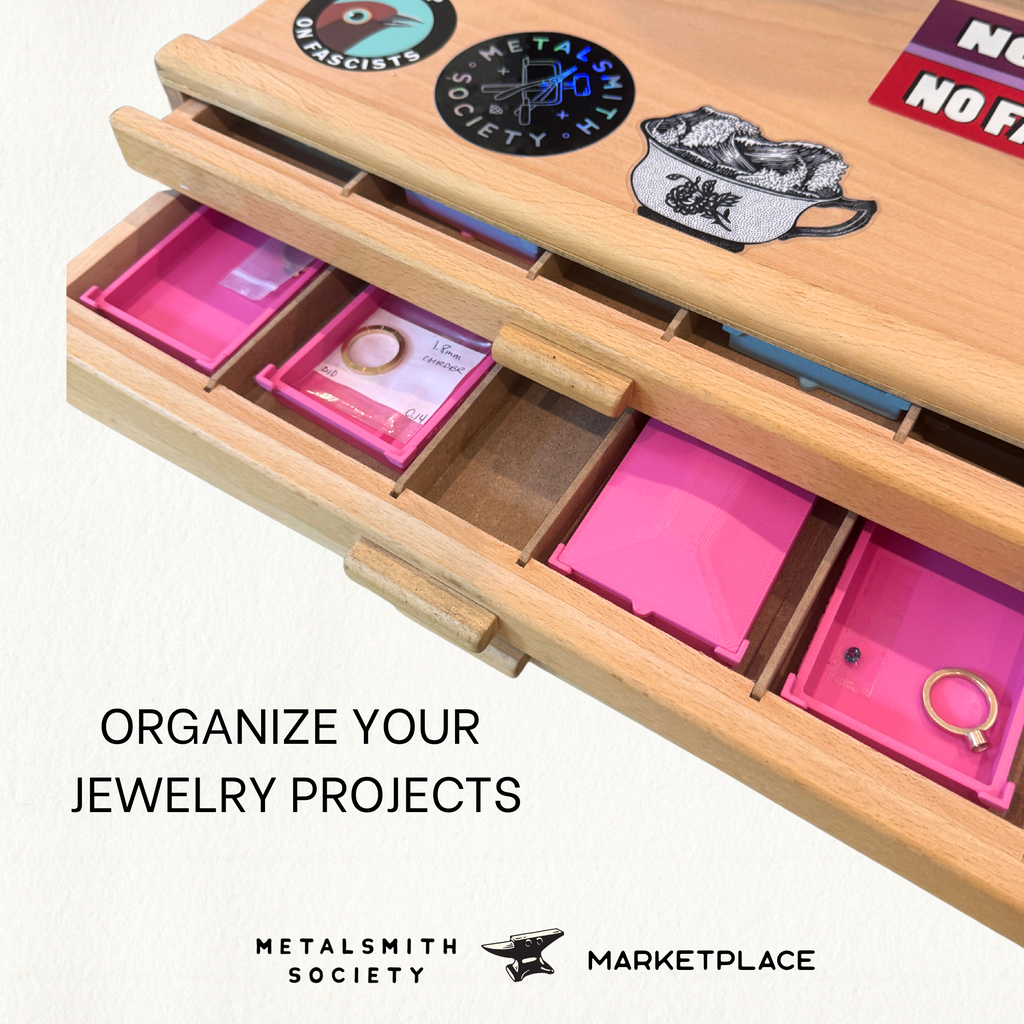 Lion Punch Forge nesting bench trays in pink neatly stored within a wooden jewelry bench box, organizing projects, gemstones, and metal pieces.