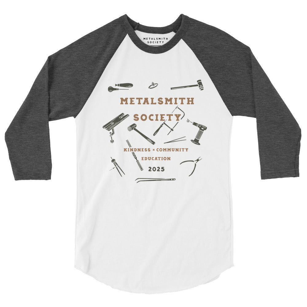 Front View of Shirt: A front-facing image of the 2025 Society Raglan Shirt featuring a white body with contrasting heather grey raglan sleeves. The Limited Edition 2025 Metalsmith Society's logo is prominently displayed on the chest with illustrations of jewerlry tools.